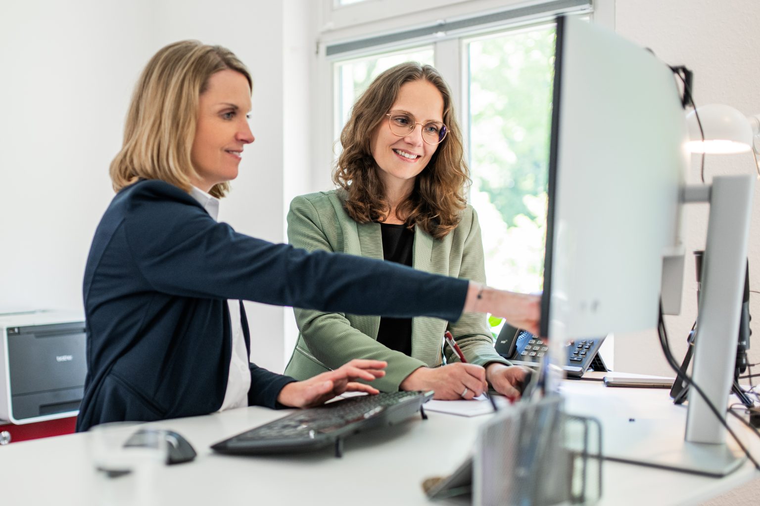 Mitarbeiterin zeigt neuer Kollegin Programme auf dem Bildschirm