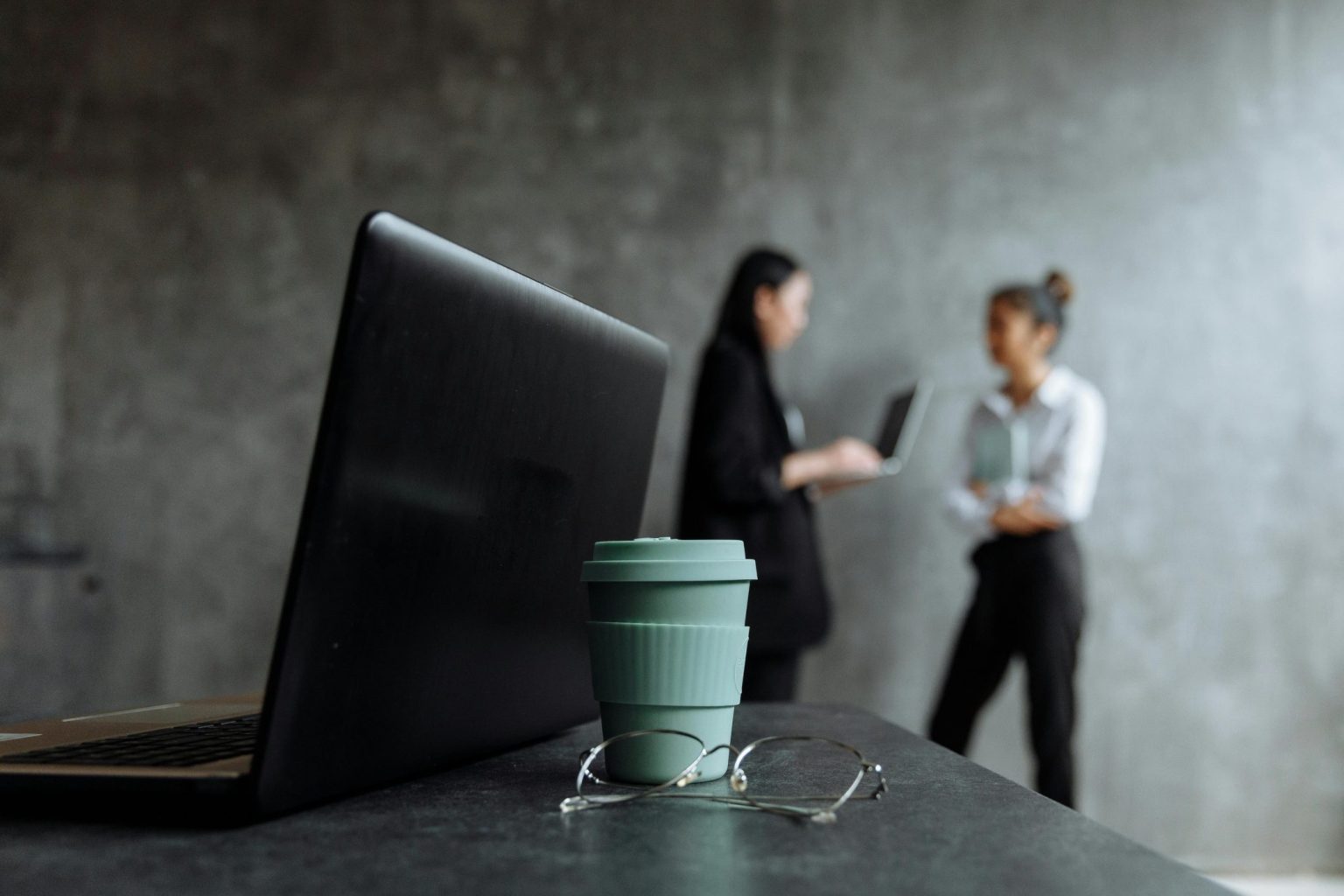 Zwei Frauen in Geschäftskleidung führen Gespräch mit Laptop im Hintergrund. Die moderne Büroszene symbolisiert digitales Recruiting von Führungskräften.