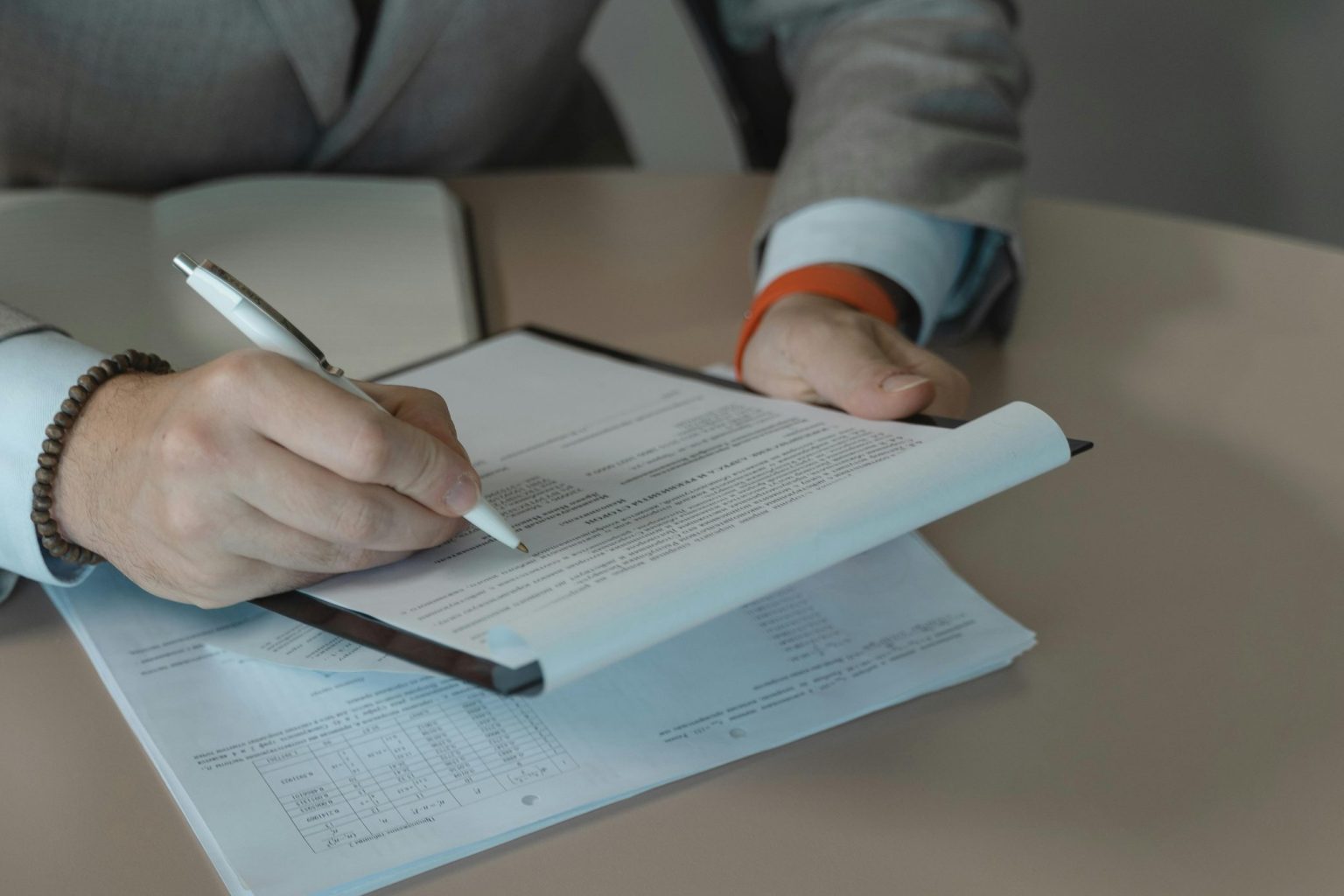 Person im Business-Outfit hält einen Stift und überprüft schriftliche Unterlagen am Tisch und verdeutlicht den strategischen Rechercheansatz bei der Identifikation von Führungskräften im Active Sourcing.