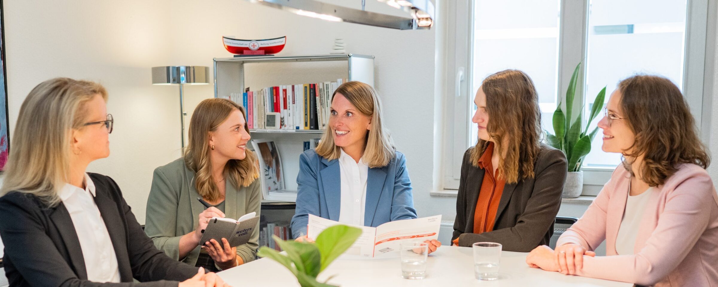 Teammitglieder von Wefers & Coll sitzen beisammen an einem Meetingtisch